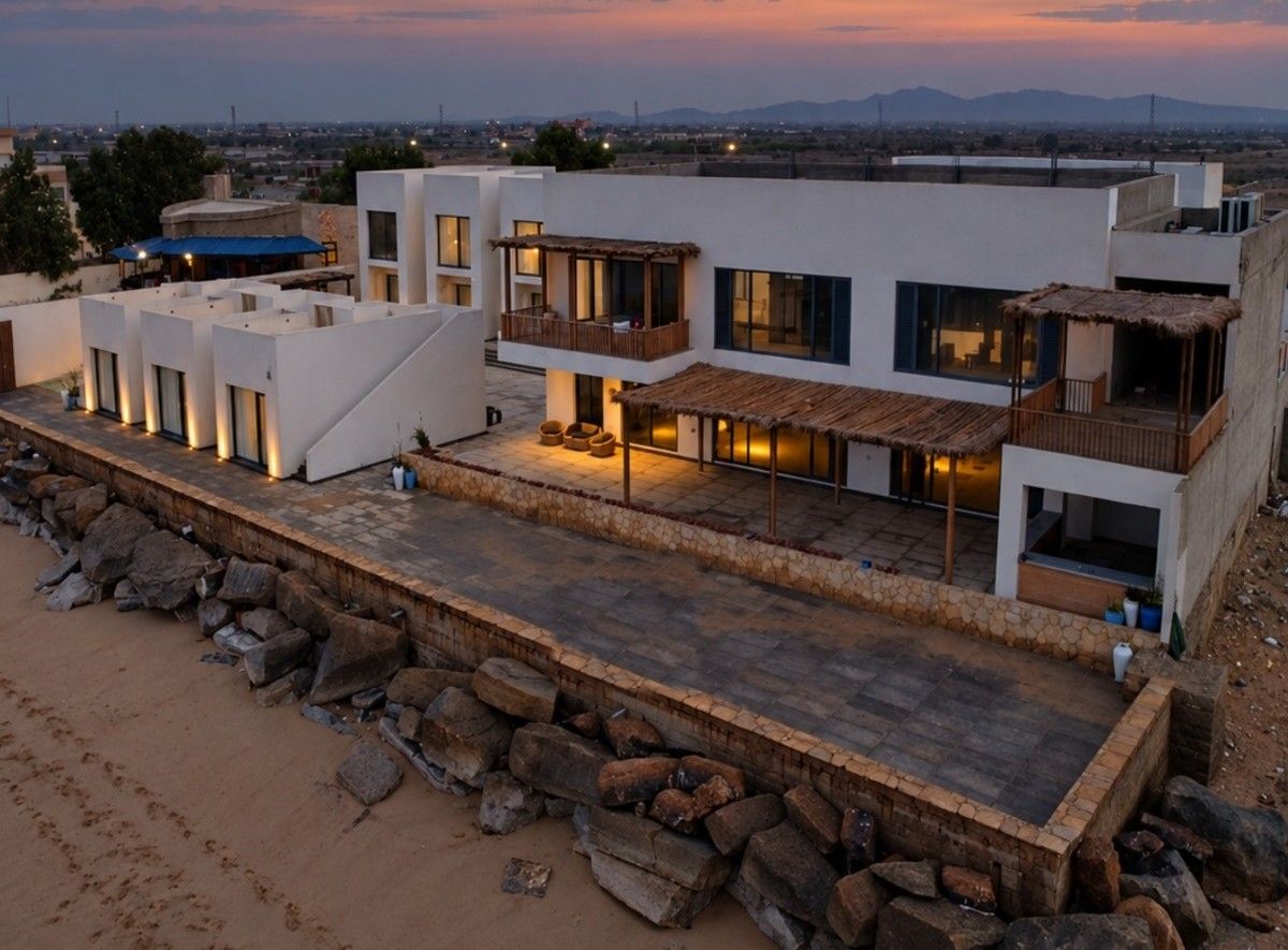 Aerial view of the Pelagos at dusk: sculpted plaster architecture, pergolas and the seafront terrace above the beach