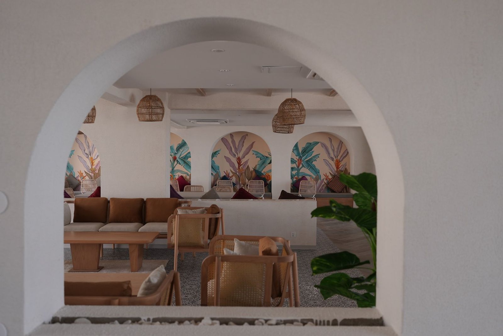 View through a plaster arch into the café, with rattan lanterns and botanical murals