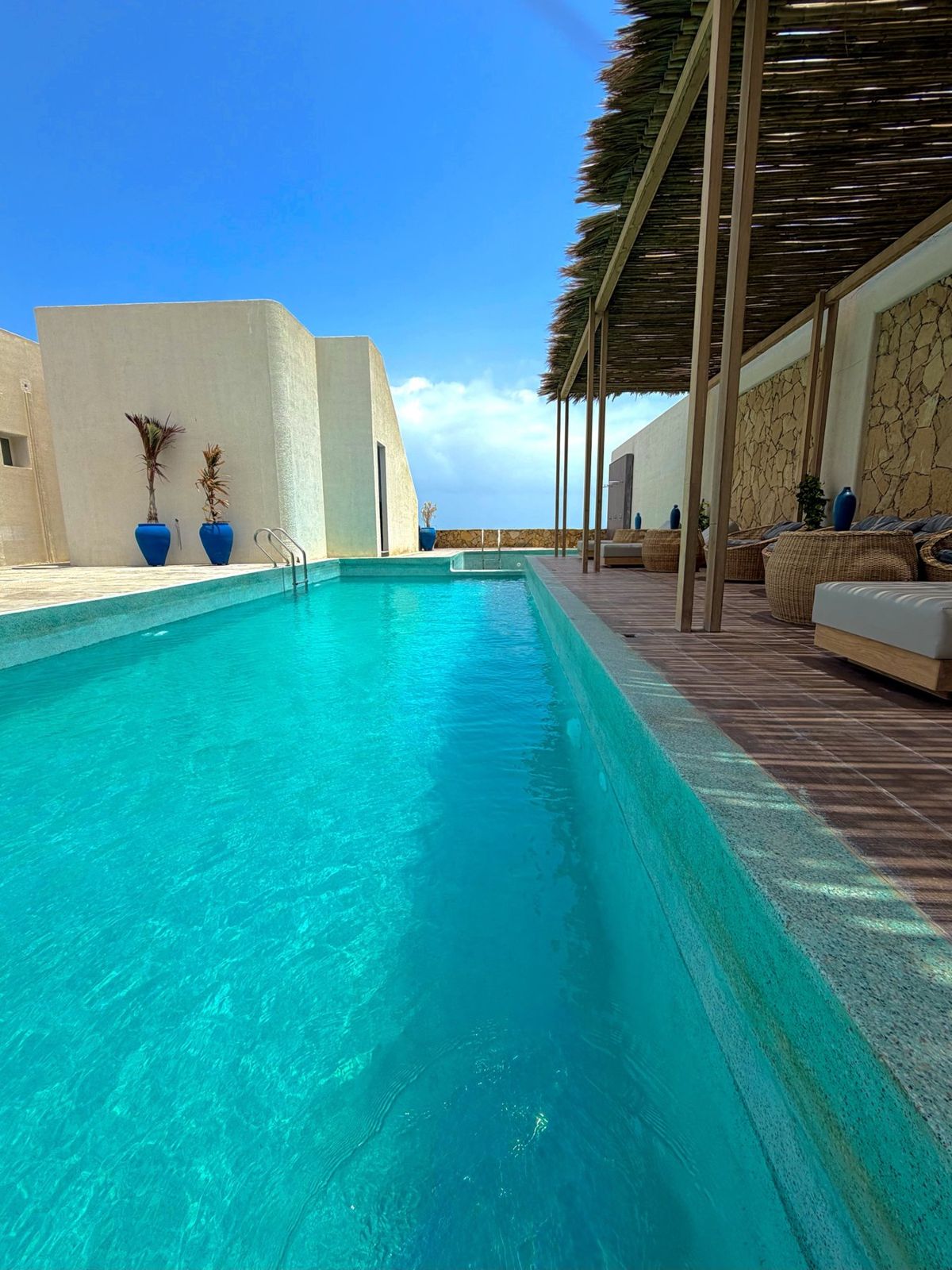 Pool deck with a thatched pergola and wicker seating
