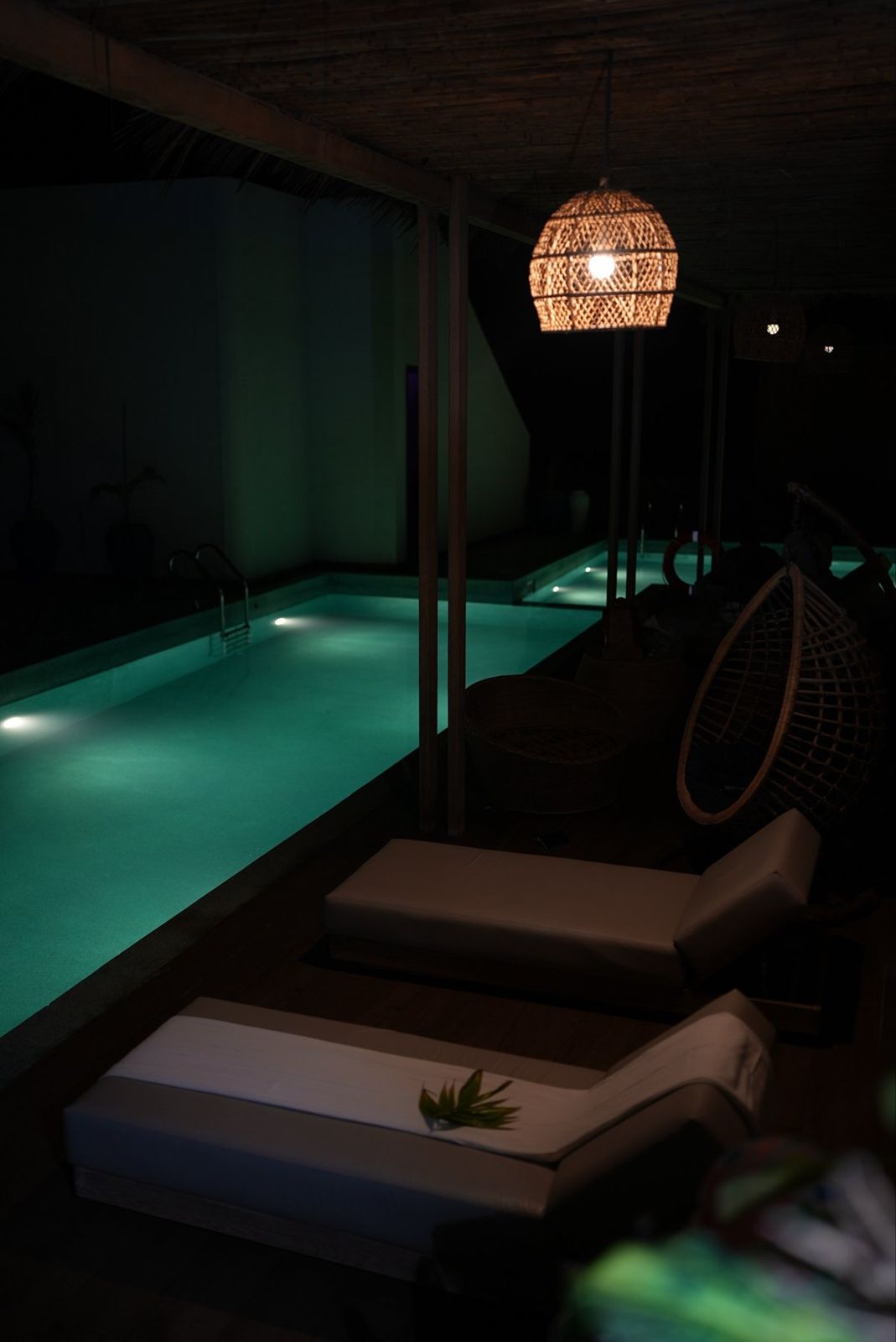 Pool at night beside loungers under a rattan lantern