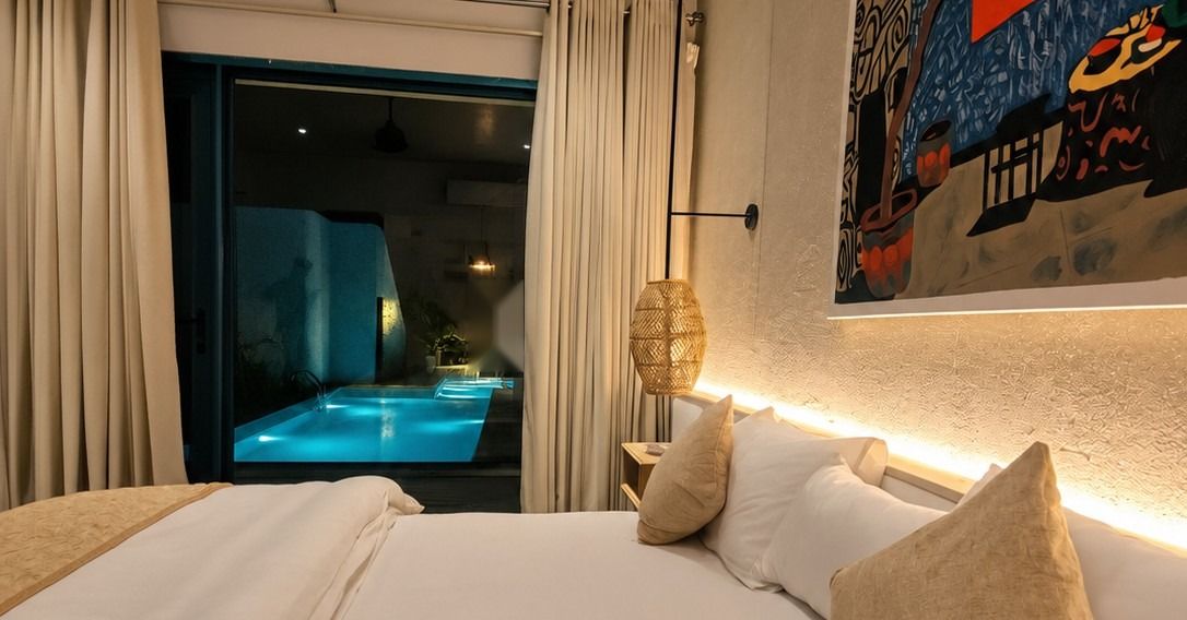 Guest room with linen bedding and original art, opening onto a lit pool
